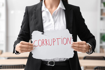 Poster - Female teacher holding paper with word CORRUPTION in classroom, closeup