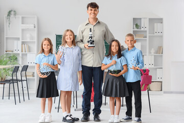 Male Chemistry teacher with microscope and little pupils in classroom