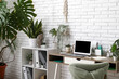 © Pixel-Shot - Workplace with blank laptop and green plants near white brick wall in office