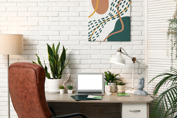 Poster - Workplace with blank laptop, lamps and green plants near white brick wall in office