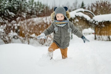 Wall Mural - Adorable little boy having fun on snowy winter day. Cute child wearing warm clothes playing in a snow.