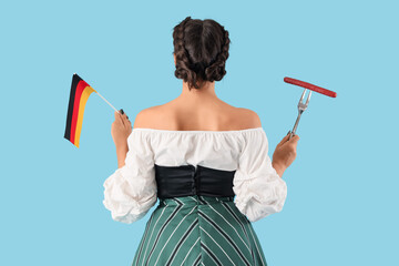 Canvas Print - Young Octoberfest waitress with sausage and German flag on blue background, back view