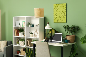 Wall Mural - Stylish workplace with laptop, shelving unit and different houseplants near green wall at home