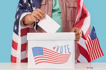 Wall Mural - Voting mature man with USA flags near ballot box at table on blue background, closeup