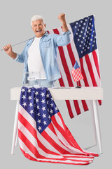 Wall Mural - Voting mature man with USA flags near ballot box at table on light background