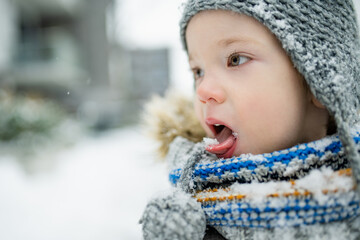 Wall Mural - Adorable little boy having fun in a city on snowy winter day. Cute child wearing warm clothes playing in a snow.