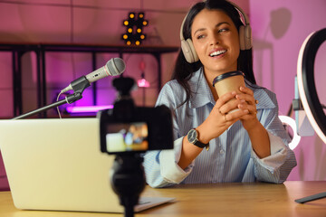 Wall Mural - Female blogger with coffee cup recording video at home in evening