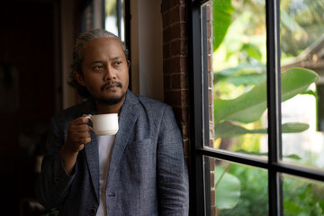 A man in a suit holding a coffee cup and looking out the window. Scene is contemplative and relaxed. lifestyle photo concept. there is copy space for ad writing
