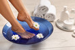 © New Africa - Woman soaking her feet in bowl with water and flowers on floor, closeup. Body care