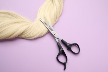 Canvas Print - Blonde hair strand and professional scissors on violet background, top view