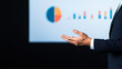 © Gibster - A speaker gesturing with hands while presenting data on screen, showcasing pie chart and bar graph. presentation conveys professionalism and engagement