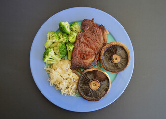 A porterhouse steak with mushrooms broccoli and sauerkraut.