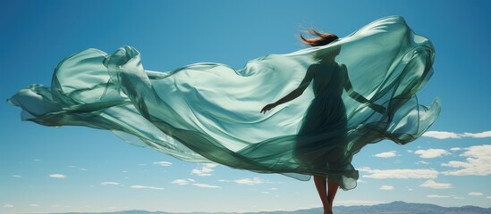 A woman jumping on green grass with flying lime-green fabric on a beautiful blue sky background.