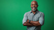 © Cavad - The image shows a joyful and confident black man standing with his arms crossed against a green screen background. His expression is warm, radiating happiness and pride. The subject is elegantly dress