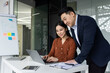 © Liubomir - Asian business professionals engaged in collaborative work environment. Colleagues discuss project details using laptop and charts. Emphasis on teamwork, productivity, and modern office atmosphere.