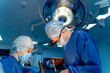 © Vadim - Surgeons in a high-tech hospital. Two surgeons in surgical attire work intently during a surgical procedure under a bright operating room light.
