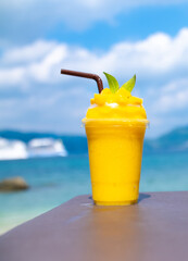 Smoothie made from fresh mango fruits against the backdrop of a seascape. Fruit and yoghurt ice cream decorated with leaves. Glass of tropical dessert close-up.