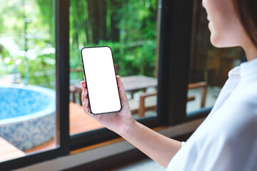 Wall Mural - Mockup image of a woman holding mobile phone with blank desktop white screen at home