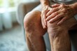 © id512 - elderly person experiencing knee pain, holding swollen joint with hands while seated at home, close-up of aging skin and arthritis symptoms