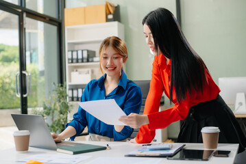 ￼￼Two young Asian professionals engaged in teamwork and business discussions in modern office