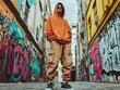 © Rudsaphon - Confident Urban Youth in Vibrant Streetwear Exploring Graffiti Covered Alley