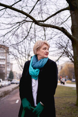 portrait of a stylish old woman in a black coat with green accessories on a spring street