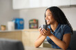 © Antonioguillem - Happy black woman drinking coffee looking away in the kitchen