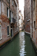 Narrow Venetian canal between weathered buildings with aged facades. This photo captures the essence of Venice's historic architecture and is ideal for travel imagery and cultural storytelling.