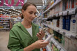 © Grustock - Young woman selecting cosmetics in a supermarket while using a smartphone to compare prices and read reviews, making informed decisions about her beauty purchases