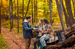 © Zoran Zeremski - Three friends resting after hiking in forest sitting on collapsed trunk and drinking tea.