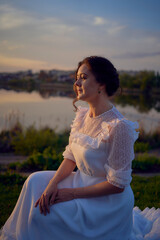 a woman in a white vintage dress on the shore of a lake at sunset