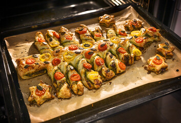 Baked savory Christmas tree fresh from the oven from puff pastry filled with green pesto and decorated with tomato slices on a baking tray, creative holiday meal, copy space