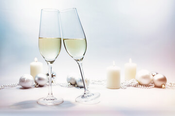 Two champagne glasses toast for New Year, bright background with candles, Christmas baubles and snowy bokeh, copy space, selected focus