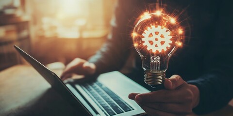 Fototapete - A man holds a light bulb with a gear icon inside while using a notebook computer, representing the inspiration for innovative ideas through online technology.