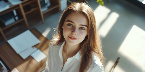 Poster - A woman with long brown hair is smiling at the camera. She is wearing a white shirt and is sitting at a desk