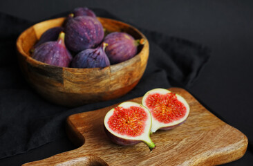 Ripe whole and sliced ​​figs on a wooden board on a dark background