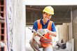 © Robert Kneschke - Portrait of smiling young female bricklayer taking cement on trowel from bucket while plastering wall at construction site