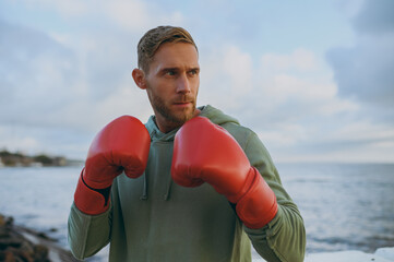 Wall Mural - Close up young cool strong sporty athletic toned fit sportsman man wear sports clothes red gloves boxing warm up training at sunrise sun dawn over sea beach outdoor on seaside in summer day morning