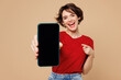 © ViDi Studio - Young happy woman she wear red t-shirt casual clothes hold in hand use point finger on mobile cell phone with blank screen workspace area isolated on plain pastel beige background. Lifestyle concept.