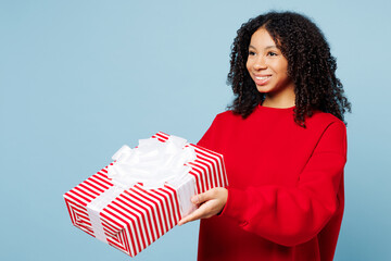 Wall Mural - Side view little happy fun kid teen girl of African American ethnicity wear red sweatshirt hold present box with gift ribbon bow isolated on pastel plain blue background. Childhood lifestyle concept.