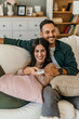 © La Famiglia - Shot of a beautiful mid adult happy couple sitting on a couch at home and watching tv