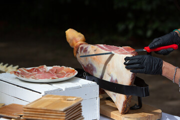 Waiter slicing iberian ham from a leg on a wooden table for outdoor catering event