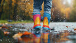 © Milla - Young child wearing colorful rain boots standing in a puddle on a rainy autumn day.