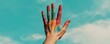 © kamon - A vibrant hand raised against a clear blue sky, showcasing colorful paint splashes, symbolizing creativity and self-expression.