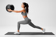 © nikolas_jkd - Active girl doing lunges exercises for leg muscle training. Fitness woman doing front forward one leg step lunge exercise with med ball
