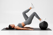 © nikolas_jkd - Athletic girl doing glute bridge exercise with med ball on gray background. Fitness woman working out