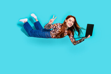 Wall Mural - Full body photo of pretty young girl flying hold netbook show v-sign wear trendy colorful outfit isolated on aquamarine color background