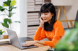 © David - asian woman is sitting on a white couch in a modern home. Her is smiling and looking at her laptop freelance business online concept.