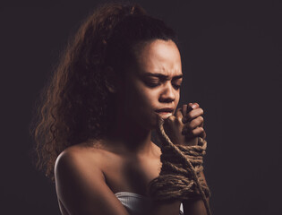 Scared woman, hands and tie with rope for kidnapping, hostage or slavery on a dark studio background. Young, female person or victim in binding or praying for help, save or hero in human trafficking