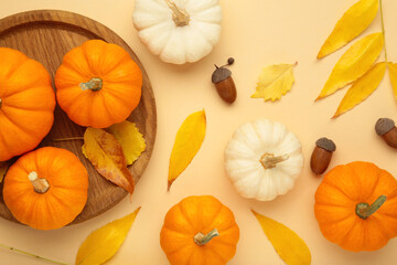 Autumn composition. Fresh orange and white pumpkin on wooden plate with autumn leaves on beige background. Top view